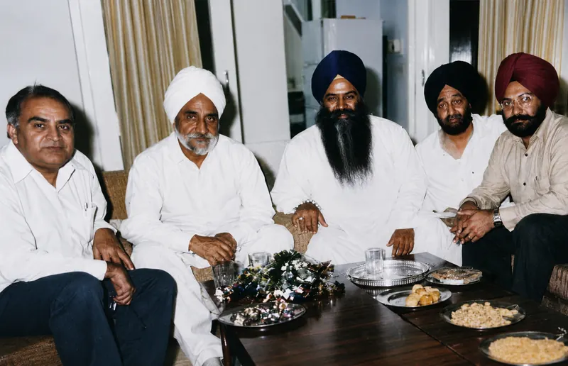 Seated at home with Darbara Singh and three others, garlands and sweets on the table before them.