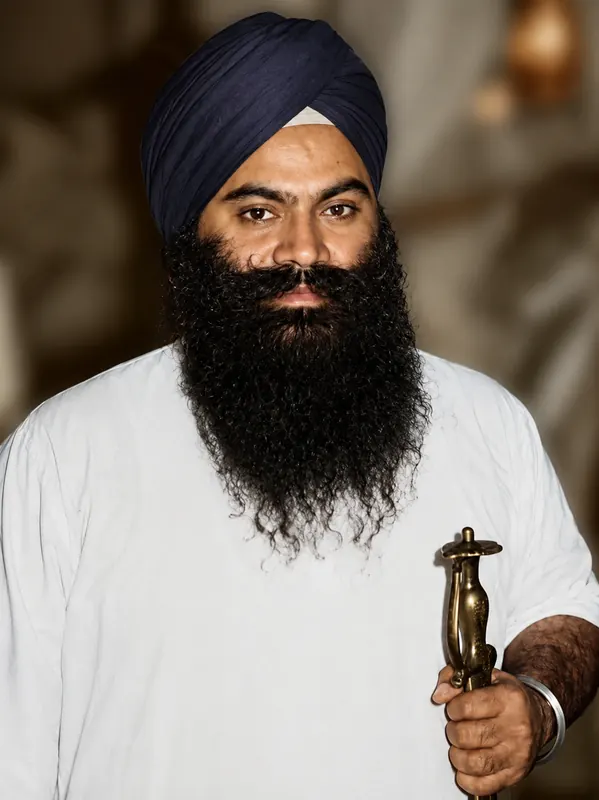 Portrait in a navy dastaar and white kurta, holding a kirpan.