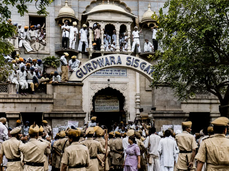 Crowds massed on the facade and balconies of Gurdwara Sis Ganj Sahib, with police ranks assembled in the street below.